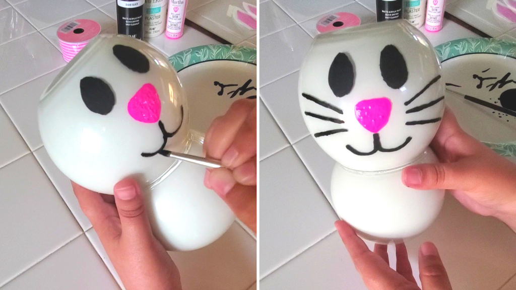 Want to make some Easter decorations to add some cute bunny decor to your home? Learn how to create this easy decorative DIY Glass Jar Easter Bunny craft using dollar store glass jars and paint for a fun Easter decor idea!
For the bunny's mouth, paint a line with the black paint underneath the nose and create two curved lips stemming from that line, and add whiskers to either side of the face. 